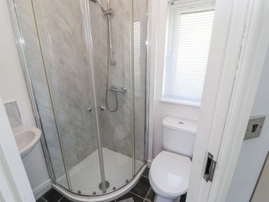 A small bathroom with a corner shower unit a toilet a window with blinds and a small wall-mounted sink at Duckling Lodge South Lakeland Leisure Village