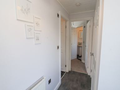 A hallway with doors leading to other rooms and framed pictures on the wall at Duckling Lodge in South Lakeland Leisure Village