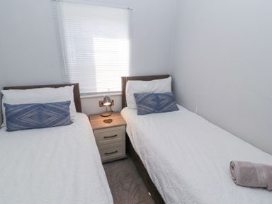A bedroom with two single beds a nightstand with a lamp and a window with blinds at Duckling Lodge in South Lakeland Leisure Village