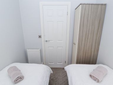 A small bedroom with two single beds each with a rolled towel a door in the center and a wardrobe on the right at Duckling Lodge in South Lakeland Leisure Village