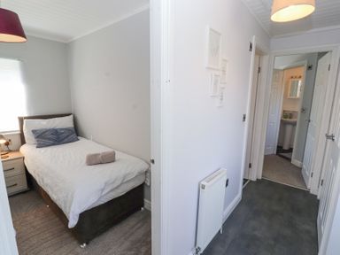 A small bedroom with a single bed next to a hallway showing doors and a bathroom at Duckling Lodge in South Lakeland Leisure Village