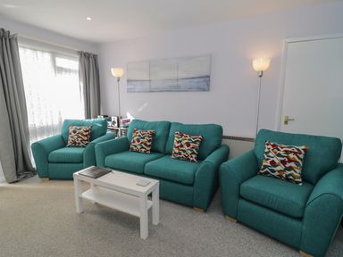 A living room with teal sofas and a white coffee table at Hafod-y-Gors in Fairbourne