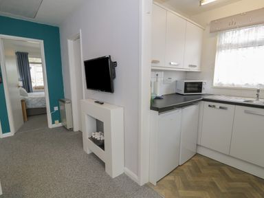 A hallway with a mounted television and a small kitchen with white cabinets and appliances at Hafod-y-Gors in Fairbourne