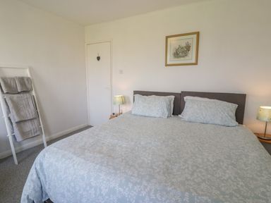 A bedroom with a double bed two lamps a framed picture towel rack and a closed door at Hafod-y-Gors in Fairbourne