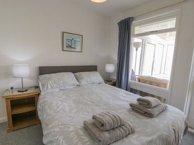 A bedroom with a double bed two bedside tables lamps picture on wall and folded towels at Hafod-y-Gors in Fairbourne