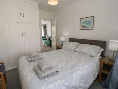 A bedroom with a double bed, bedside tables with lamps, folded towels on the bed, built-in wardrobe and a doorway to a living room at Hafod-y-Gors in Fairbourne
