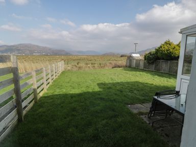 A grassy backyard with wooden and lattice fences and outdoor table and chairs at Hafod-y-Gors in Fairbourne