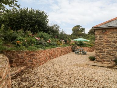 An outdoor gravel area with a stone wall garden and a picnic table with an umbrella at The Old Haybarn in Ipplepen