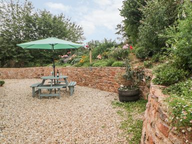 A garden area with a picnic table and umbrella surrounded by stone walls and plants at The Old Haybarn in Ipplepen