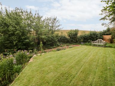 A garden with a wooden bench a grass lawn and trees and bushes at The Old Haybarn in Ipplepen
