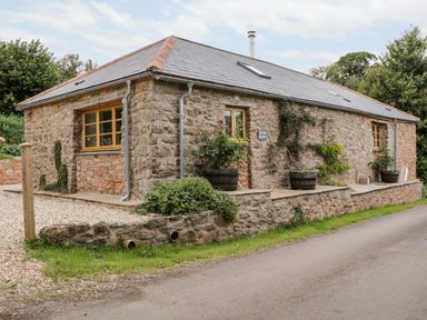 A stone house with wooden windows and potted plants outside at The Old Haybarn in Ipplepen