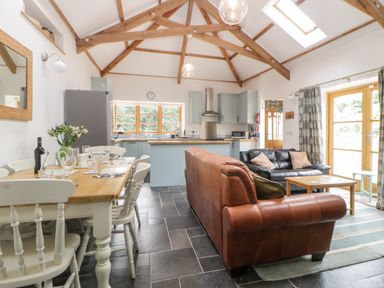 An open plan kitchen and living room with dining table chairs sofas and wooden ceiling beams at The Old Haybarn in Ipplepen