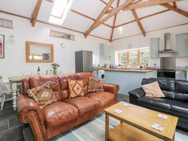 An open living room and kitchen area with brown and black leather sofas a wooden coffee table and kitchen cabinets at The Old Haybarn in Ipplepen
