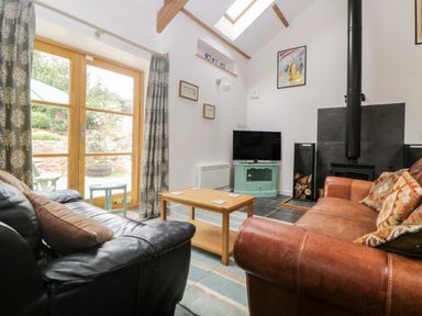 A living room with black and brown sofas a wooden coffee table a television and a wood burning stove at The Old Haybarn in Ipplepen