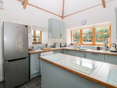 A kitchen with a refrigerator, cabinets, countertop appliances and windows at The Old Haybarn in Ipplepen