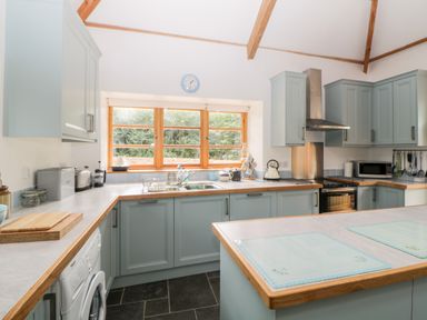 A kitchen with blue cabinets wooden countertops and a window showing greenery at The Old Haybarn in Ipplepen