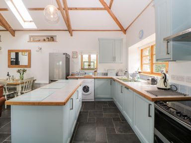 A kitchen with light blue cabinets a dining table with chairs and a refrigerator at The Old Haybarn in Ipplepen