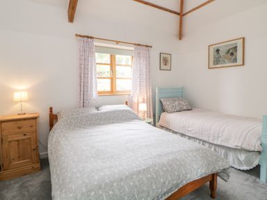 A bedroom with a double bed and a single bed under a window with curtains at The Old Haybarn in Ipplepen