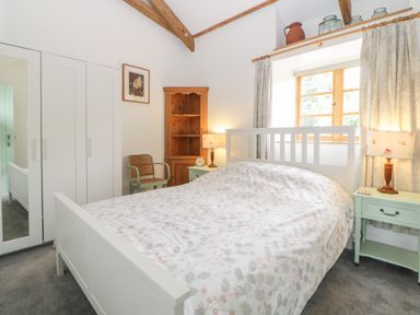A bedroom with a bed a wooden shelf two nightstands lamps a chair and a wardrobe at The Old Haybarn in Ipplepen
