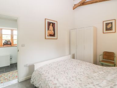 A bedroom with a bed a white wardrobe a chair and two framed pictures on the walls at The Old Haybarn in Ipplepen