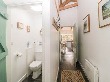 A hallway with a patterned rug and coat hooks leading to a kitchen with dining chairs and a toilet room on the left at The Old Haybarn in Ipplepen
