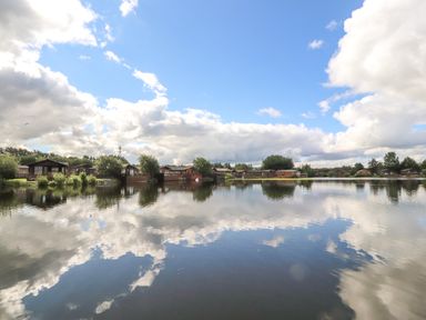 A lake with houses and trees along the shore under a cloudy sky reflecting on water at Mereside in South lakeland Leisure Village near Carnforth