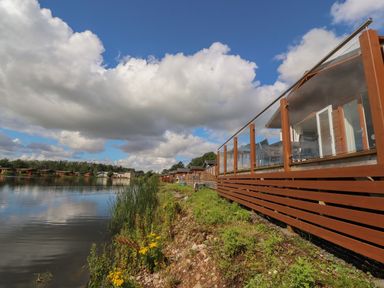 A lakeside view with wooden deck railing and houses along the shore at Mereside South lakeland Leisure Village near Carnforth