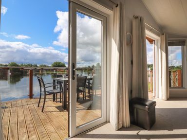 A room with large glass doors opening to a wooden deck with a table and chairs overlooking water at Mereside South lakeland Leisure Village near Carnforth