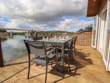An outdoor deck with a dining table and chairs overlooking a lake at Mereside South lakeland Leisure Village near Carnforth