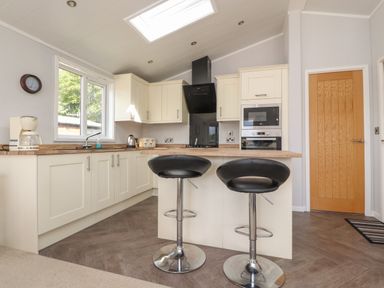 A kitchen with white cabinets and wooden countertops two black bar stools a microwave oven and a wooden door at Mereside in South lakeland Leisure Village near Carnforth