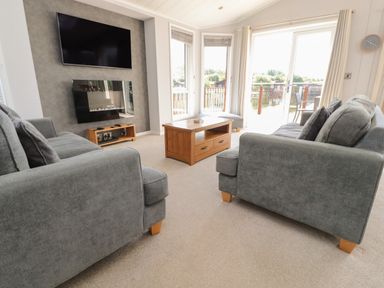 A living room with two grey sofas a wooden coffee table a wall mounted tv and a fireplace at Mereside in South lakeland Leisure Village near Carnforth