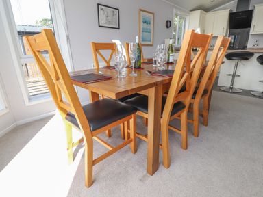 A dining room with a wooden table and six wooden chairs with black seats at Mereside South lakeland Leisure Village near Carnforth