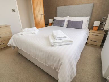 A bedroom with a double bed white linens folded towels bedside tables and lamps at Mereside South lakeland Leisure Village near Carnforth
