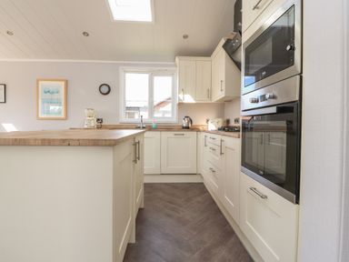 A kitchen with white cabinets wooden countertops built in oven microwave and a window at Mereside South lakeland Leisure Village near Carnforth