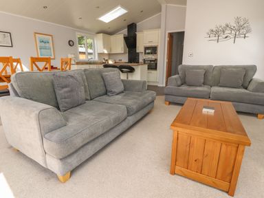 A living room with gray sofas a wooden coffee table and an open kitchen at Mereside in South lakeland Leisure Village near Carnforth