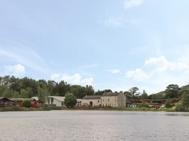 A lake with buildings and trees along the shore at Mereside South lakeland Leisure Village near Carnforth