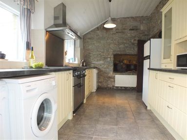 A kitchen with washing machine fridge oven and microwave with stone wall at The Farmhouse in Newport Pembrokeshire