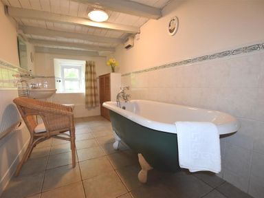 A bathroom with a freestanding bathtub a wicker chair a sink a window and a wooden cabinet at The Farmhouse Newport Pembrokeshire