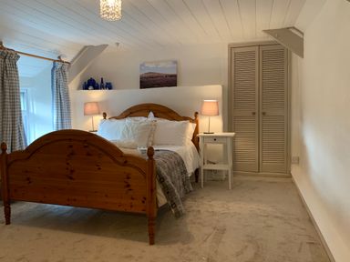 A bedroom with a wooden bed a white nightstand with a lamp a window with checked curtains and a closet at The Farmhouse in Newport Pembrokeshire
