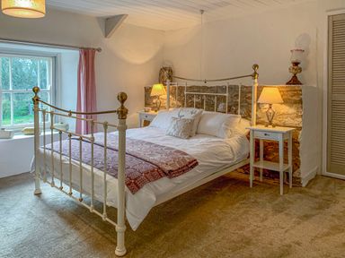 A bedroom with a metal frame bed two bedside tables with lamps a window with curtains and a stone wall at The Farmhouse in Newport Pembrokeshire