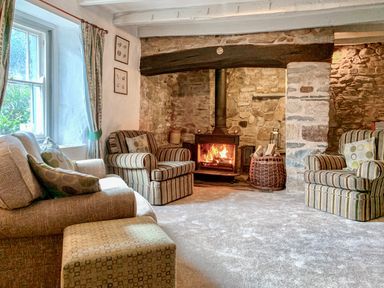 A living room with a wood-burning stove stone walls armchairs and a window at The Farmhouse in Newport Pembrokeshire