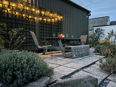 An outdoor patio with a wooden picnic table two chairs string lights and plants at The Farmhouse in Newport Pembrokeshire