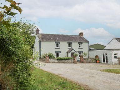 A two-story house with white walls and gray trim surrounded by plants and a gravel driveway at The Farmhouse in Newport Pembrokeshire