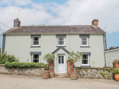 A two story house with a white door and four windows surrounded by plants and brick pillars at The Farmhouse in Newport Pembrokeshire