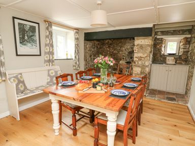 A dining room with a wooden table set for six and a bench with daisy cushions at The Farmhouse in Newport Pembrokeshire