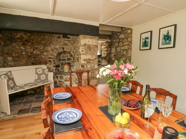 A dining room with a wooden table set with plates glasses flowers and fruit at The Farmhouse in Newport Pembrokeshire