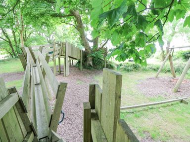 A wooden playground structure with a slide and a swing set in a wooded area at The Farmhouse in Newport Pembrokeshire