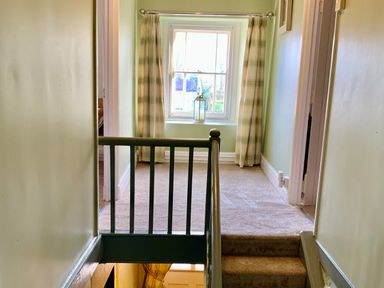 A carpeted hallway with stairs leading up to a window with plaid curtains and a lantern at The Farmhouse in Newport Pembrokeshire