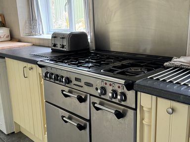 A kitchen with a stainless steel gas stove oven a toaster on the counter and cupboards below the counter at The Farmhouse in Newport Pembrokeshire