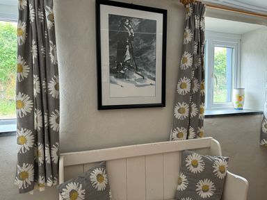 A seating area with a white wooden bench two floral cushions two windows with floral curtains and a framed picture on the wall at The Farmhouse in Newport Pembrokeshire
